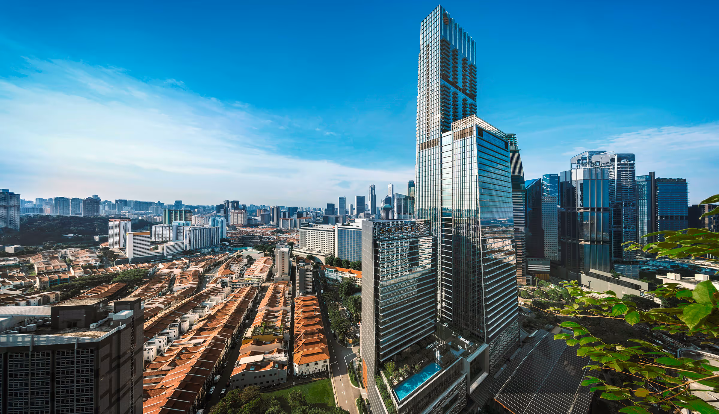Tall modern Guoco Tower skyscraper with reflective glass facade in a cityscape under a clear blue sky.