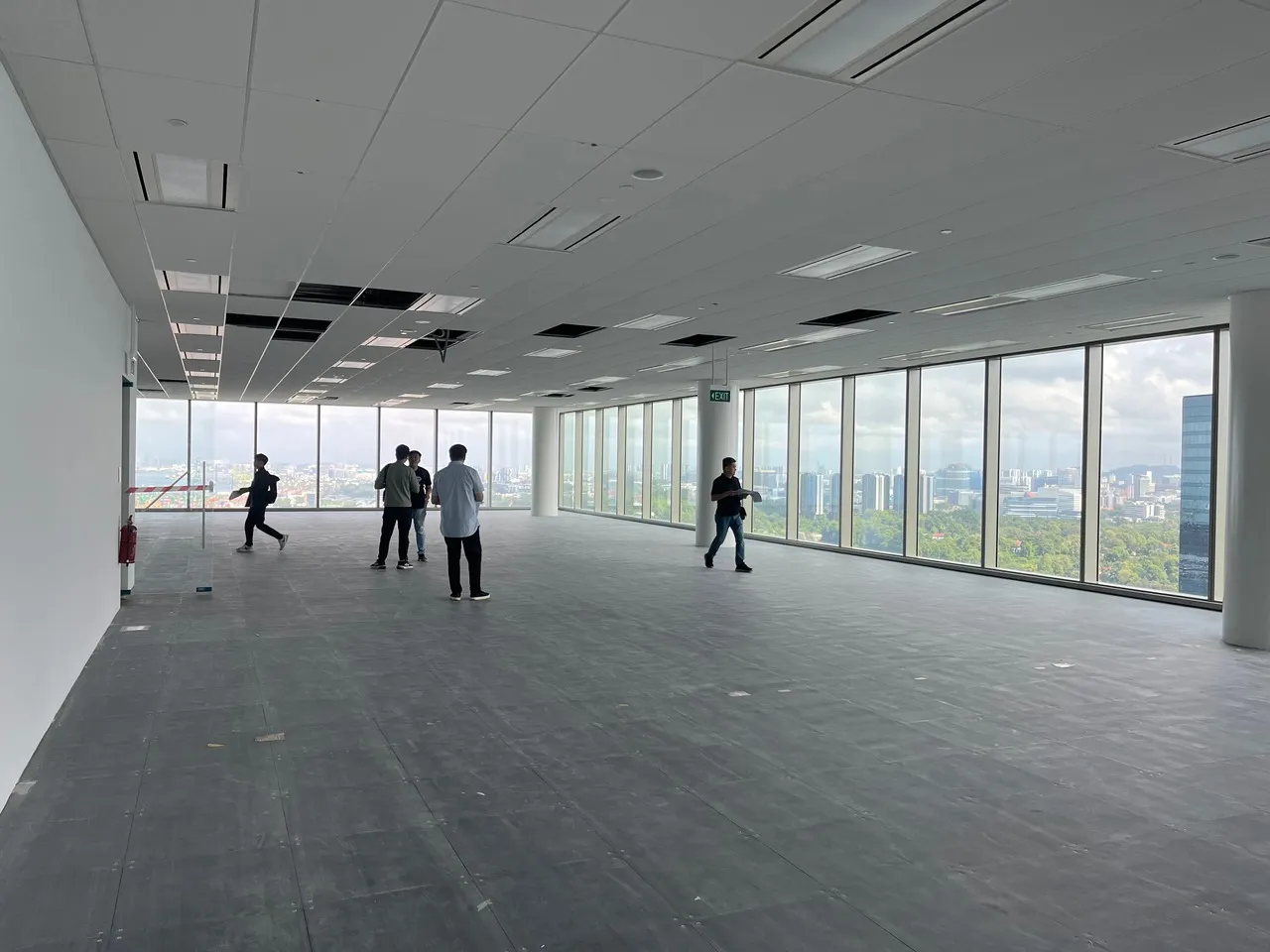 Spacious empty office space with large floor-to-ceiling windows overlooking a cityscape and five people walking inside.